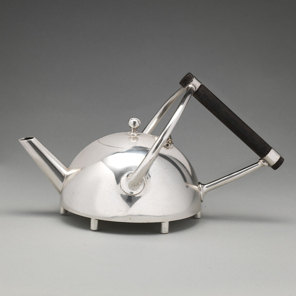 A low silver-plated teapot with an angular dark handle and straight spout.