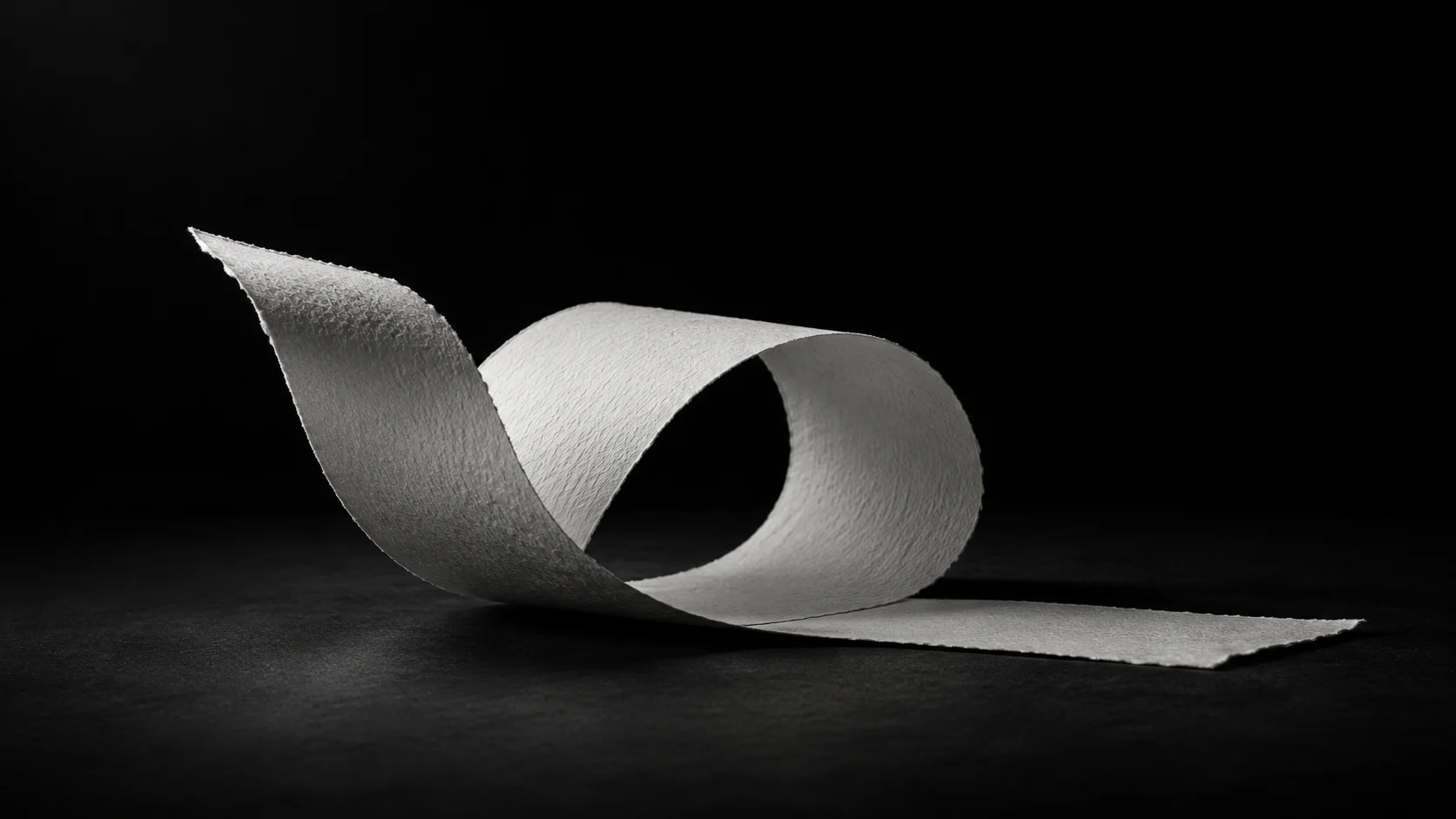 A strip of textured paper curls into an open loop, with one end lifting from the table.