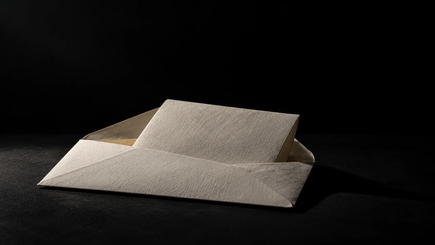An open cotton-paper envelope holds a single folded letter, lit against black.