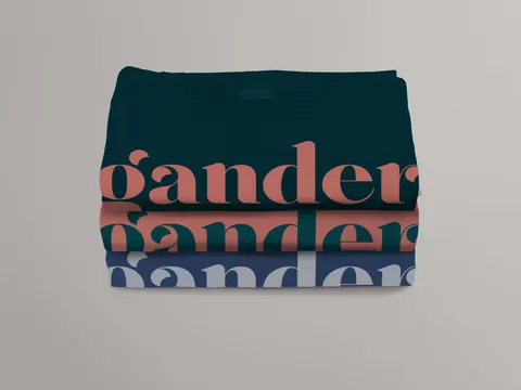 Three folded t-shirts stacked, each in a color from the Gander palette, featuring the Gander wordmark printed in bold contrasting colors.