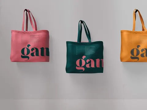 Three colorful tote bags with contrasting wrap around Gander logo hang against a plain light gray wall.